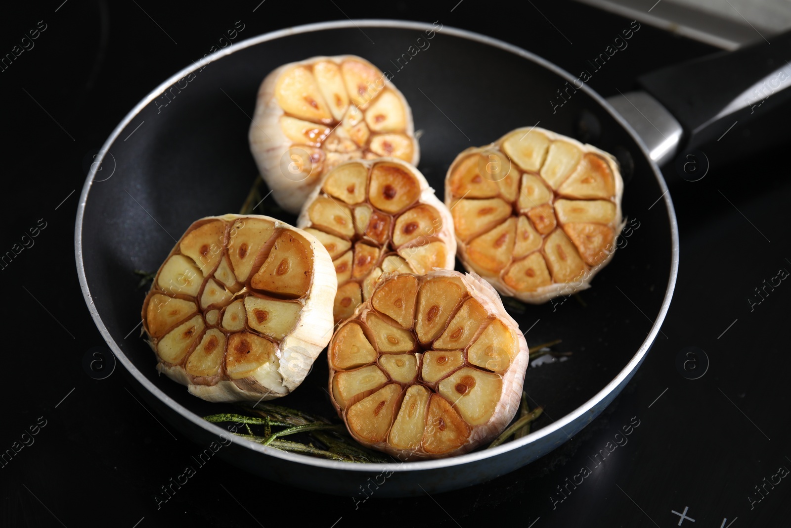 Photo of Frying pan with fried garlic and rosemary on stove, closeup