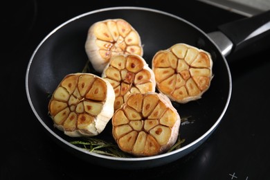 Photo of Frying pan with fried garlic and rosemary on stove, closeup
