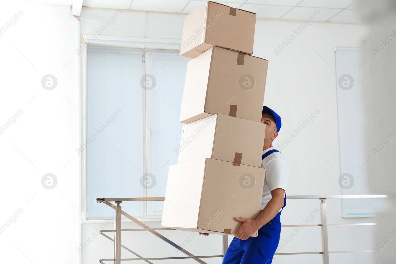 Photo of Man in uniform carrying carton boxes indoors. Posture concept