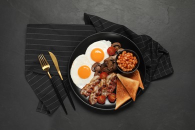 Plate with fried eggs, mushrooms, beans, bacon, tomatoes and toasted bread on black table, flat lay. Traditional English breakfast