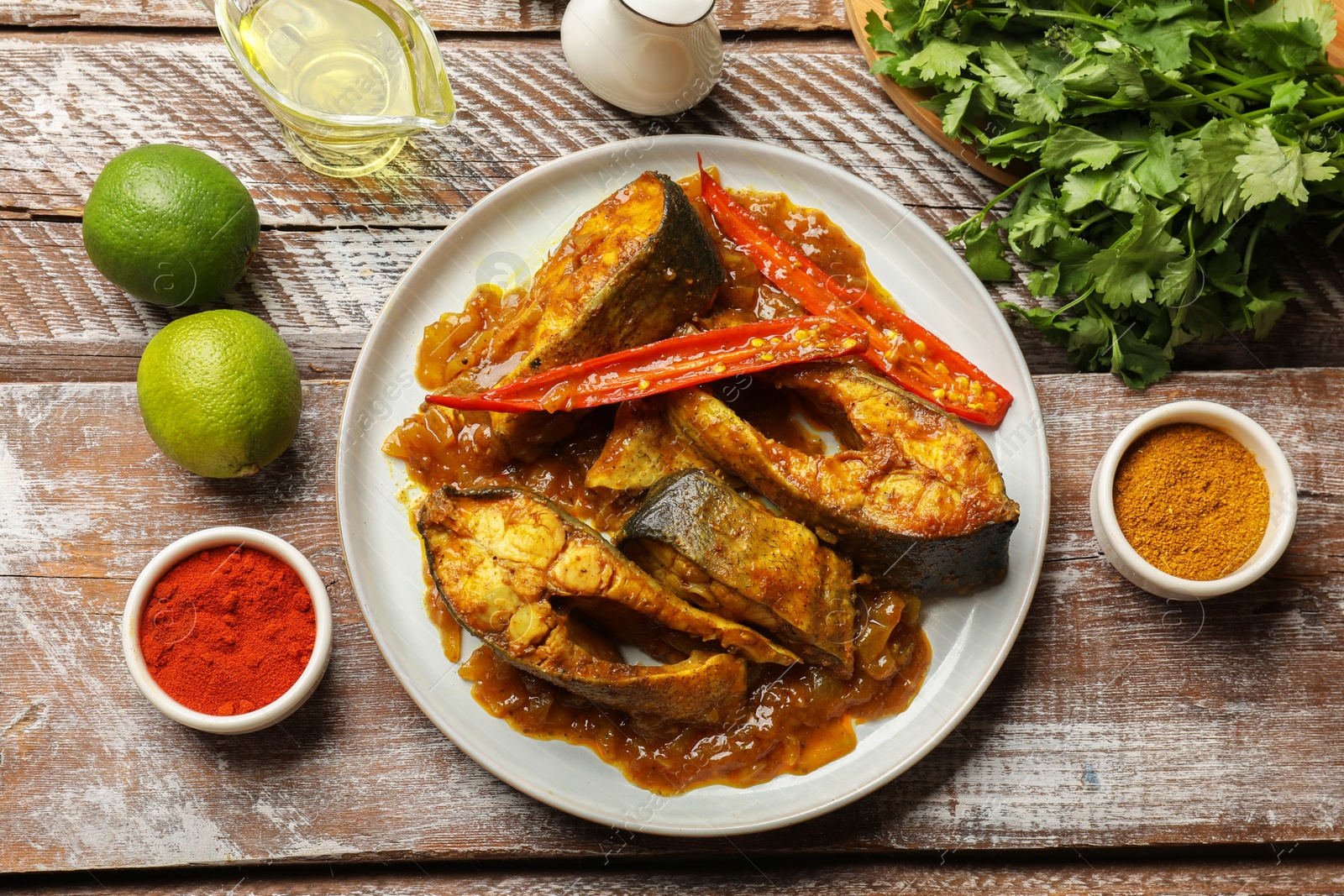 Photo of Tasty Indian fish curry on wooden table, flat lay