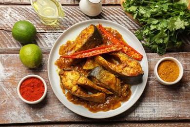 Photo of Tasty Indian fish curry on wooden table, flat lay