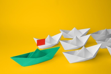 Group of paper boats following green one on yellow background. Leadership concept