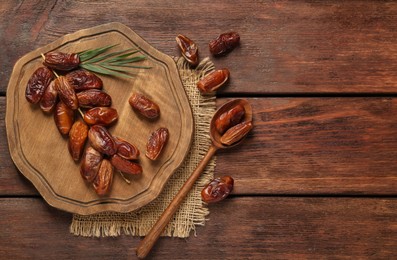 Photo of Board and spoon with tasty sweet dried dates on wooden table, flat lay. Space for text