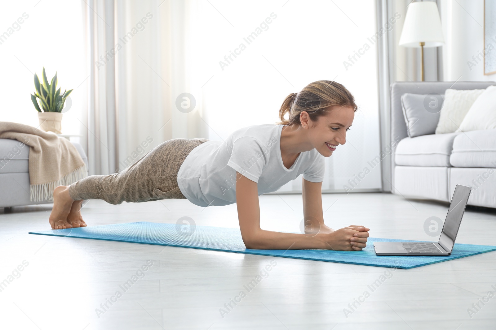 Photo of Woman having online video class via laptop at home. Distance yoga course during coronavirus pandemic