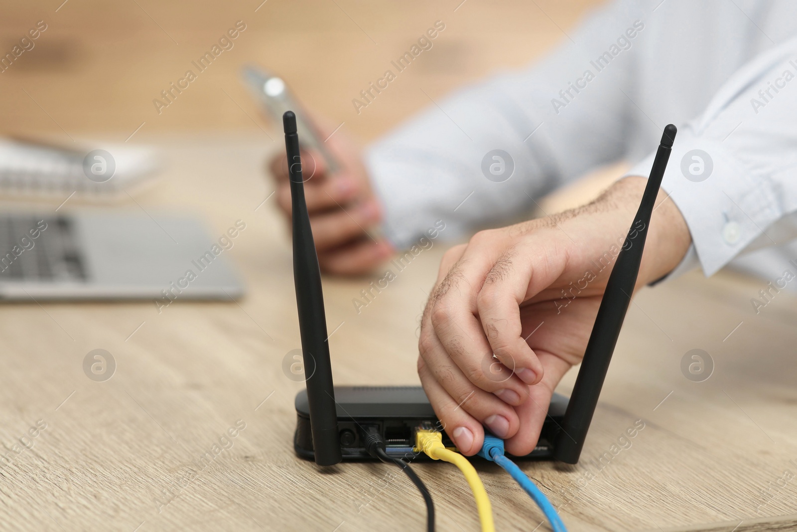 Photo of Man inserting cable into Wi-Fi router at wooden table indoors, closeup