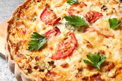 Tasty quiche with tomatoes, parsley and cheese on light table, closeup