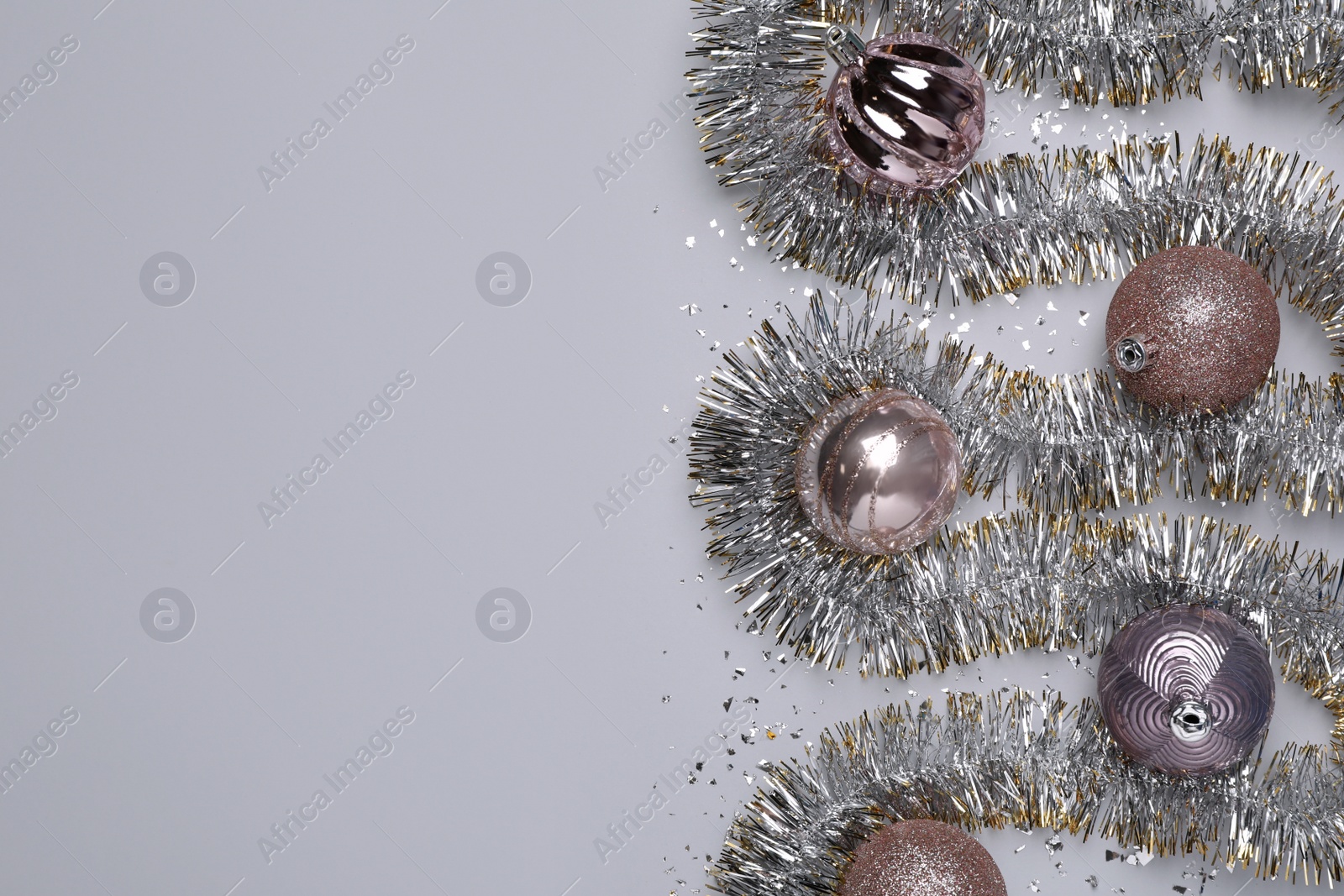 Photo of Silver tinsel, Christmas balls and confetti on light grey background, flat lay. Space for text