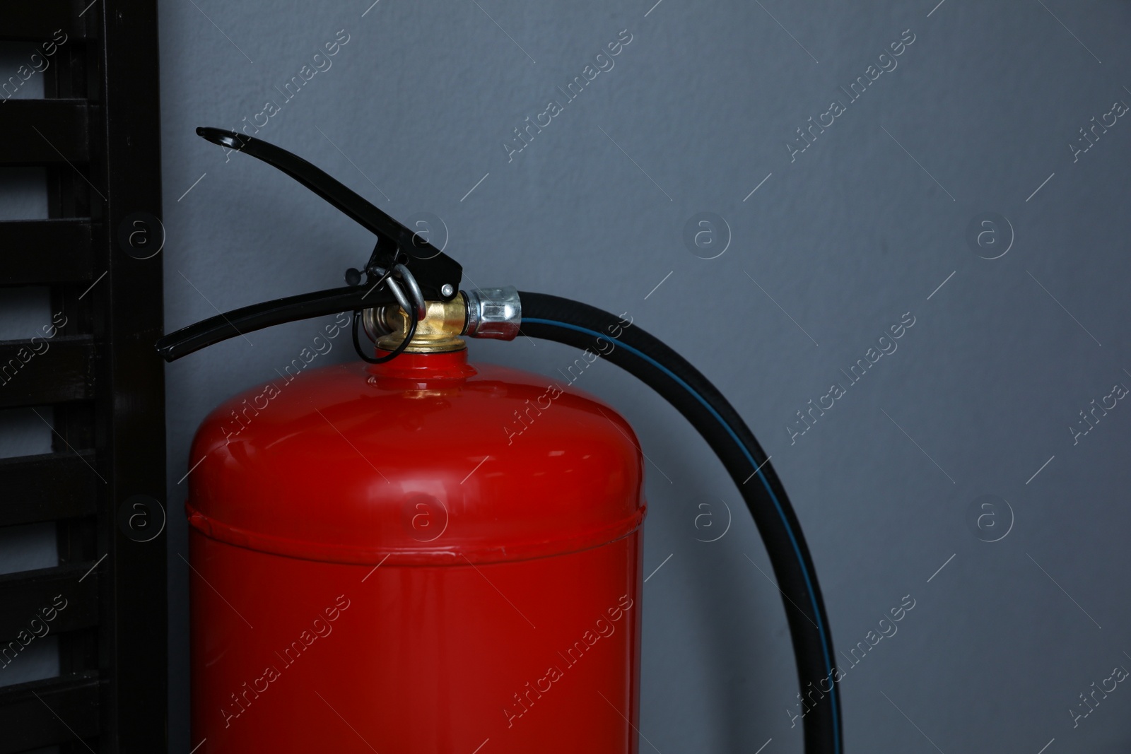 Photo of Fire extinguisher near grey wall indoors, closeup. Space for text