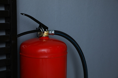 Photo of Fire extinguisher near grey wall indoors, closeup. Space for text