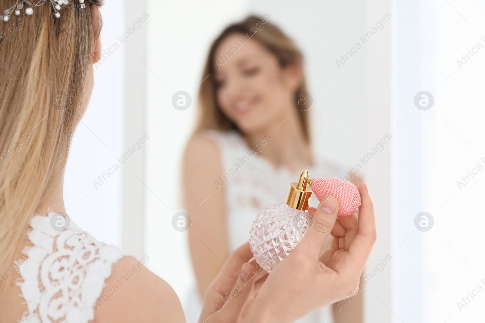 Photo of Beautiful young bride with bottle of perfume near mirror indoors