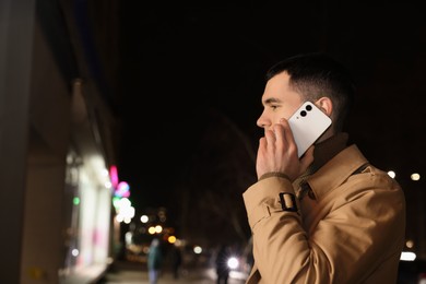 Man talking by smartphone on night city street, space for text