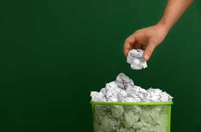 Photo of Woman throwing crumpled paper into metal bin on color background, closeup. Space for text