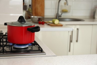 Photo of Red pot on modern kitchen stove with burning gas. Space for text