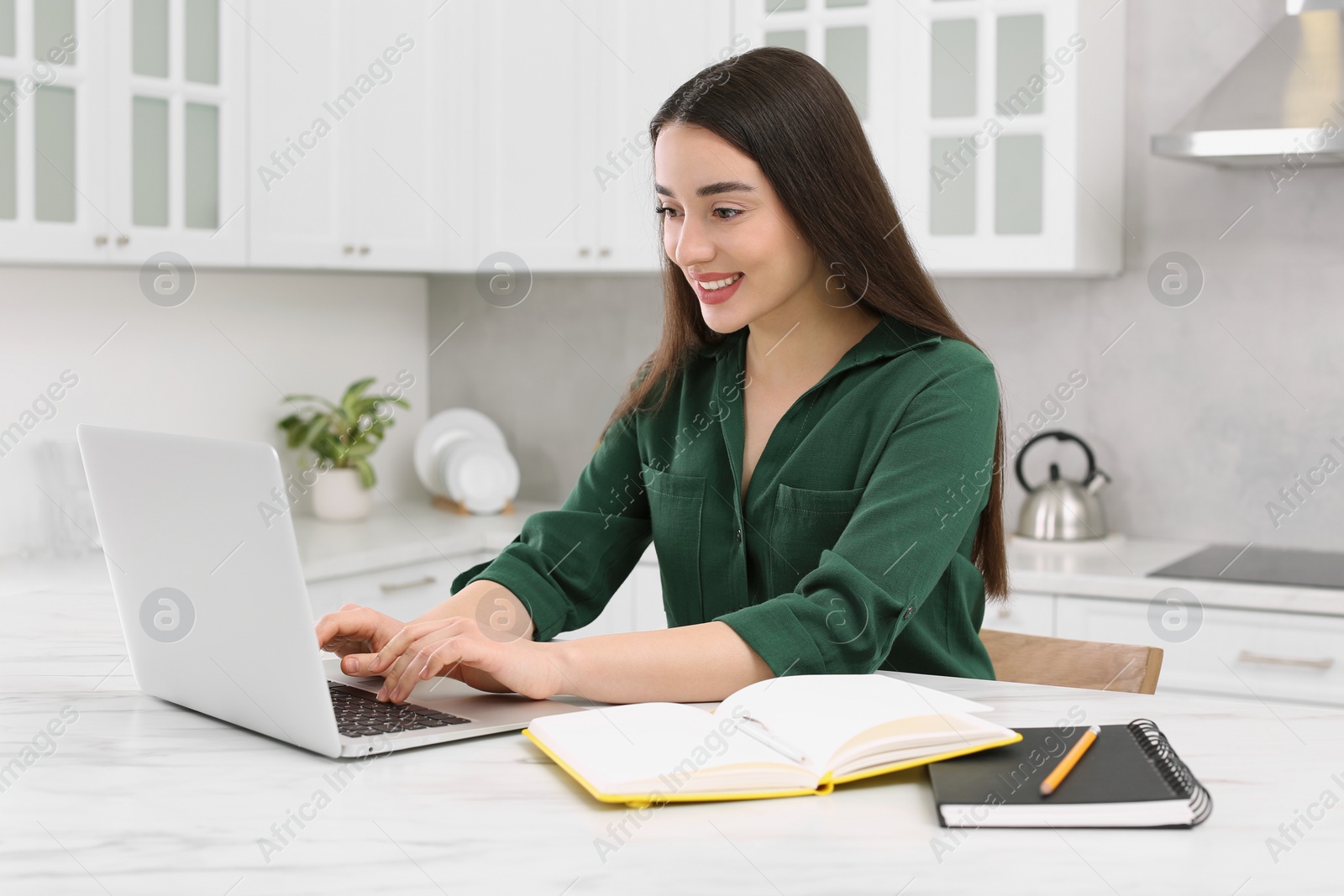 Photo of Home workplace. Happy woman typing on laptop at marble desk in kitchen