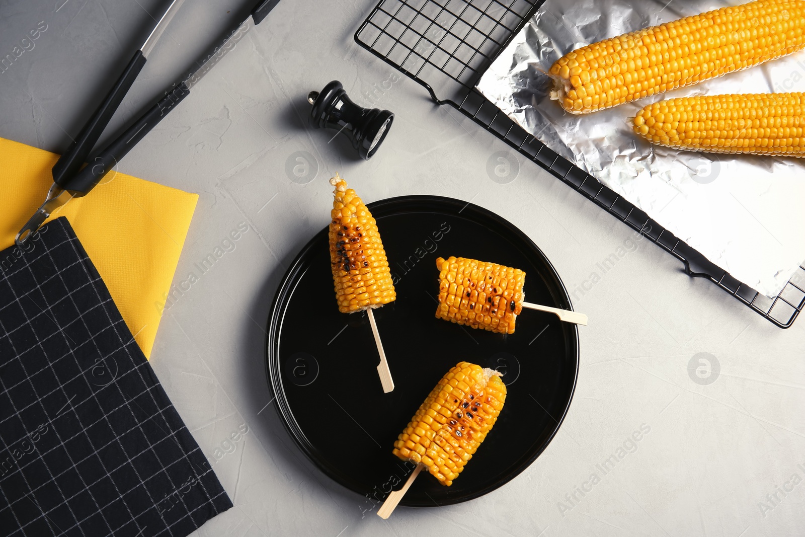 Photo of Ceramic plate with grilled corn cobs on light background, top view