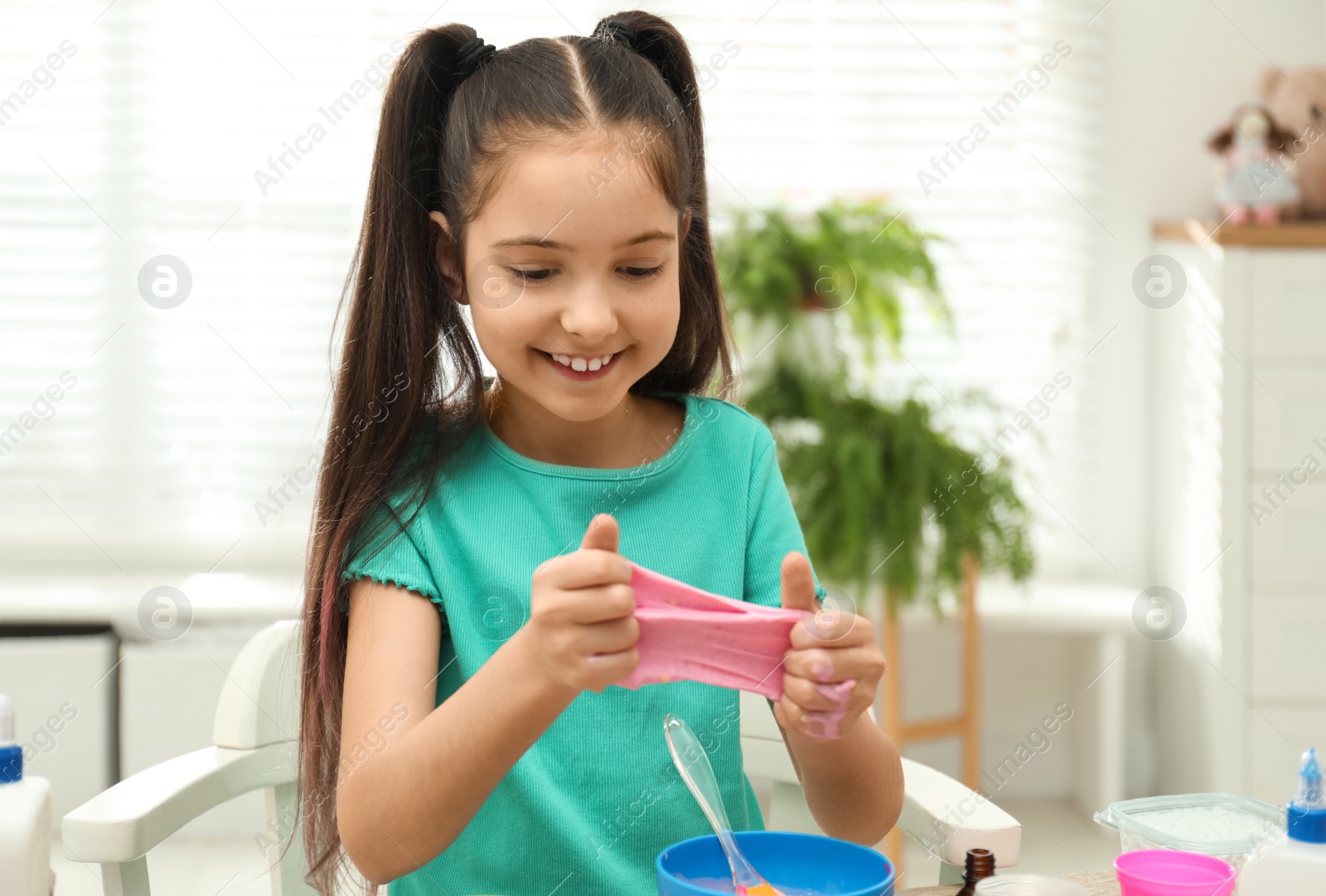 Photo of Cute little girl making DIY slime toy at table indoors