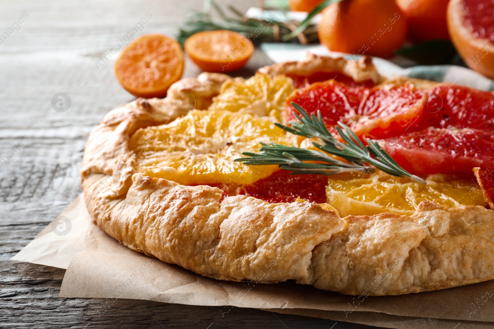Photo of Delicious galette with citrus fruits and rosemary on wooden table, closeup