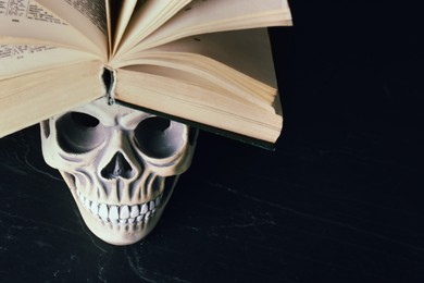 Photo of Human skull and old book on black table. Space for text