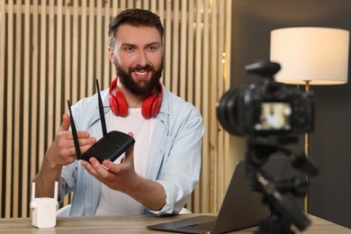 Smiling technology blogger with camera recording video review about WI-FI router at home