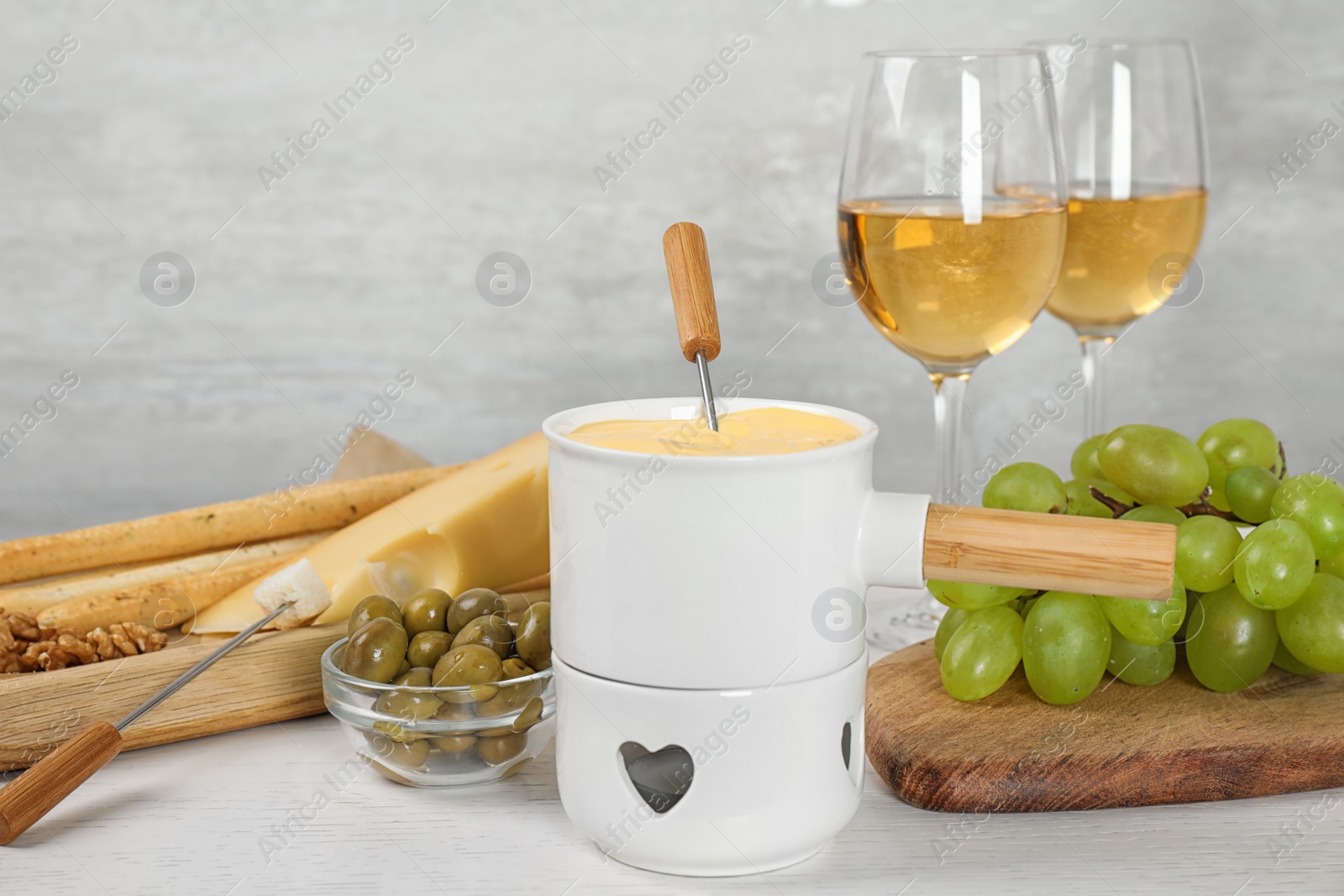 Photo of Pot of tasty cheese fondue and products on white wooden table