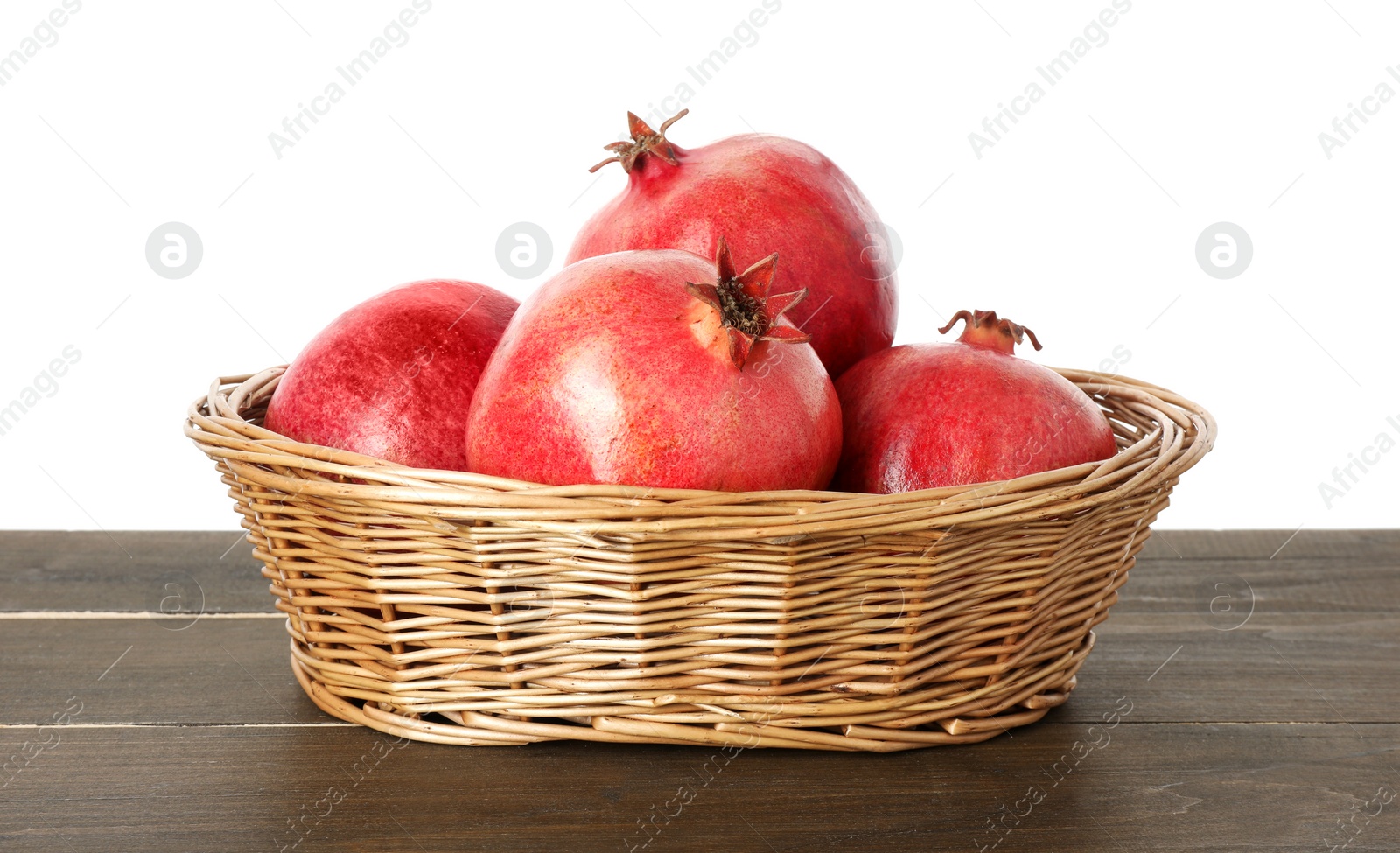 Photo of Fresh pomegranates in wicker basket on wooden table against white background