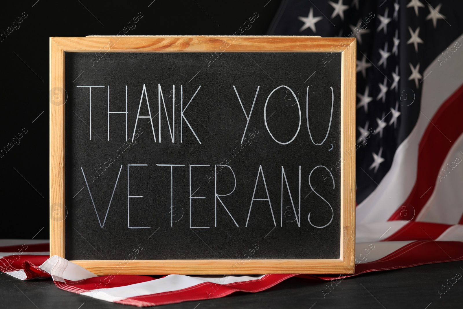 Photo of Blackboard with phrase Thank You, Veterans and American flag on grey table. Memorial Day