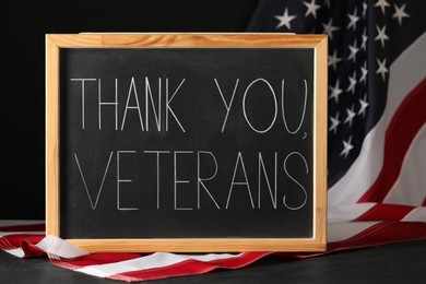 Photo of Blackboard with phrase Thank You, Veterans and American flag on grey table. Memorial Day