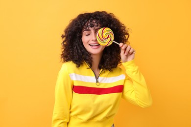 Beautiful woman covering eye with lollipop on yellow background