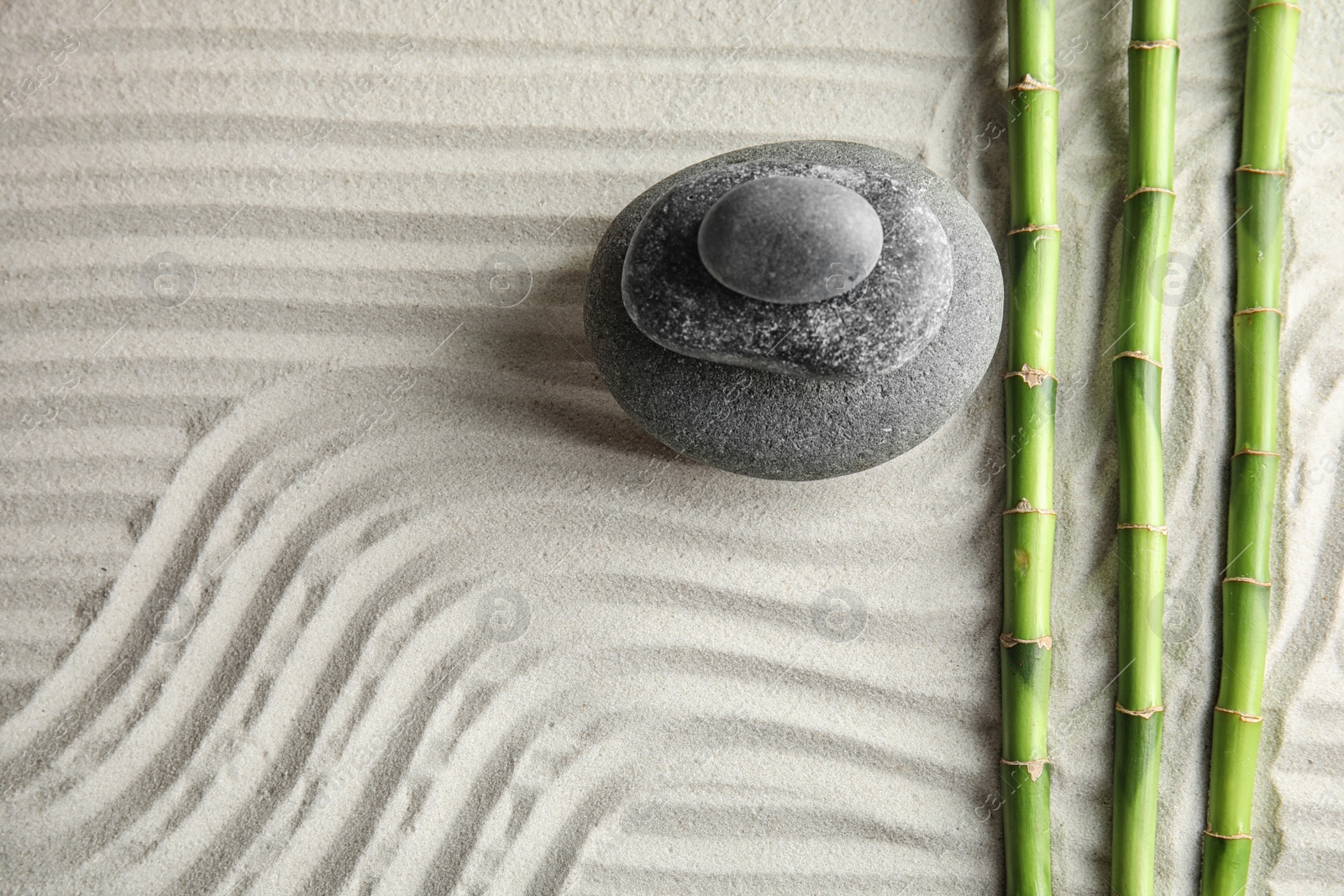 Photo of Bamboo branches with spa stones on sand, top view. Space for text