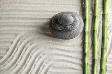 Photo of Bamboo branches with spa stones on sand, top view. Space for text