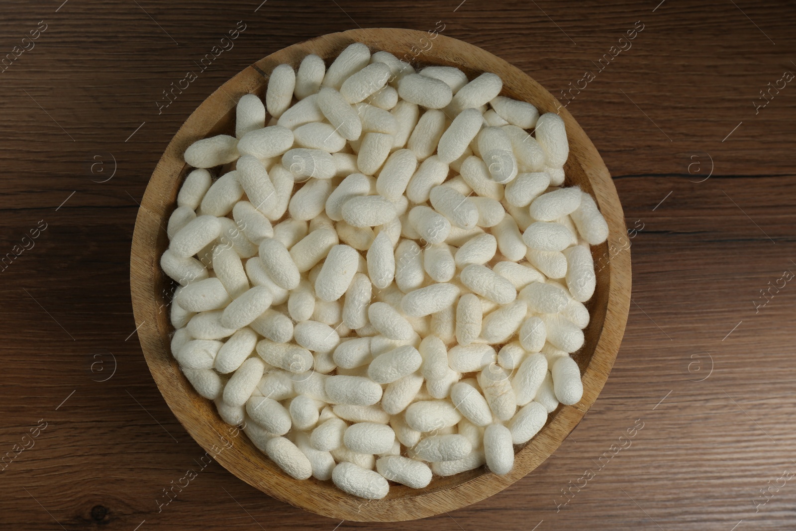 Photo of White silk cocoons in bowl on wooden table, top view