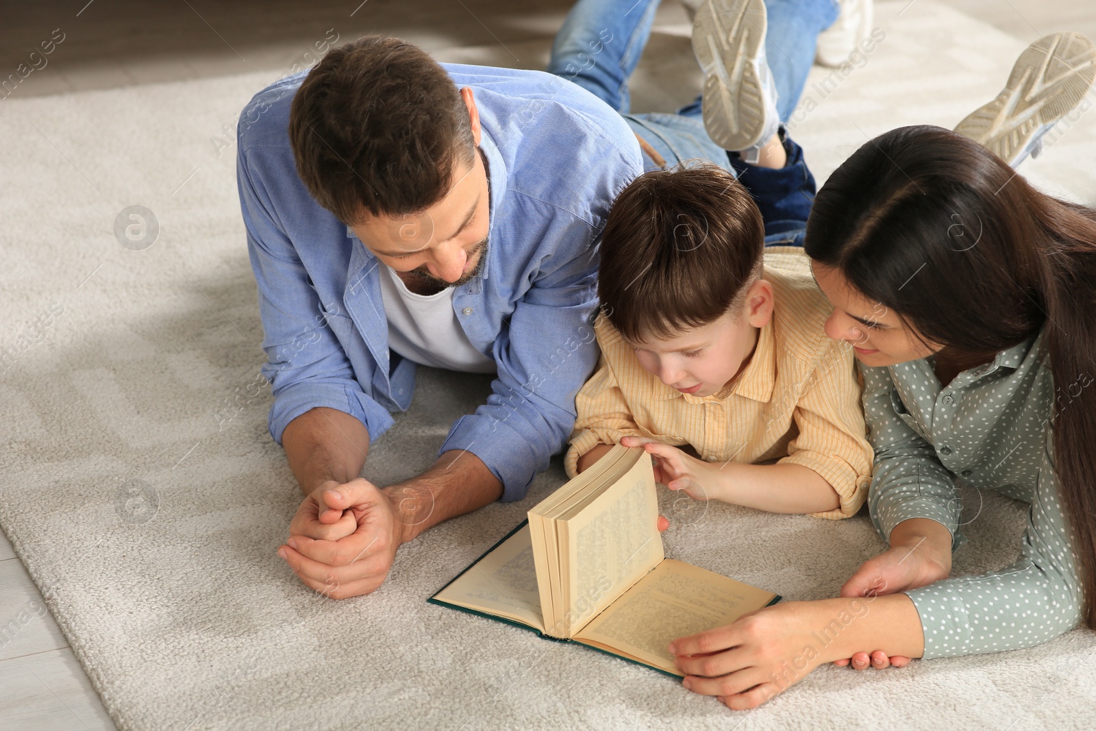 Photo of Happy family reading book together on floor in living room at home