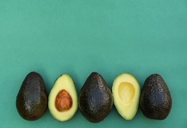 Photo of Tasty whole and cut avocados on turquoise background, flat lay. Space for text