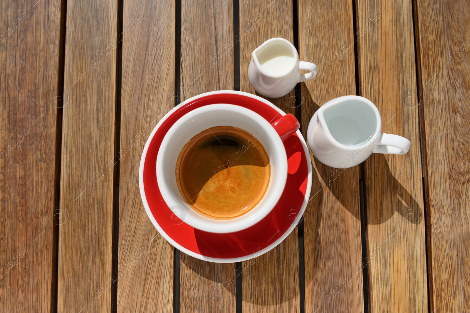 Photo of Cup of aromatic hot coffee, milk and water on wooden table, flat lay