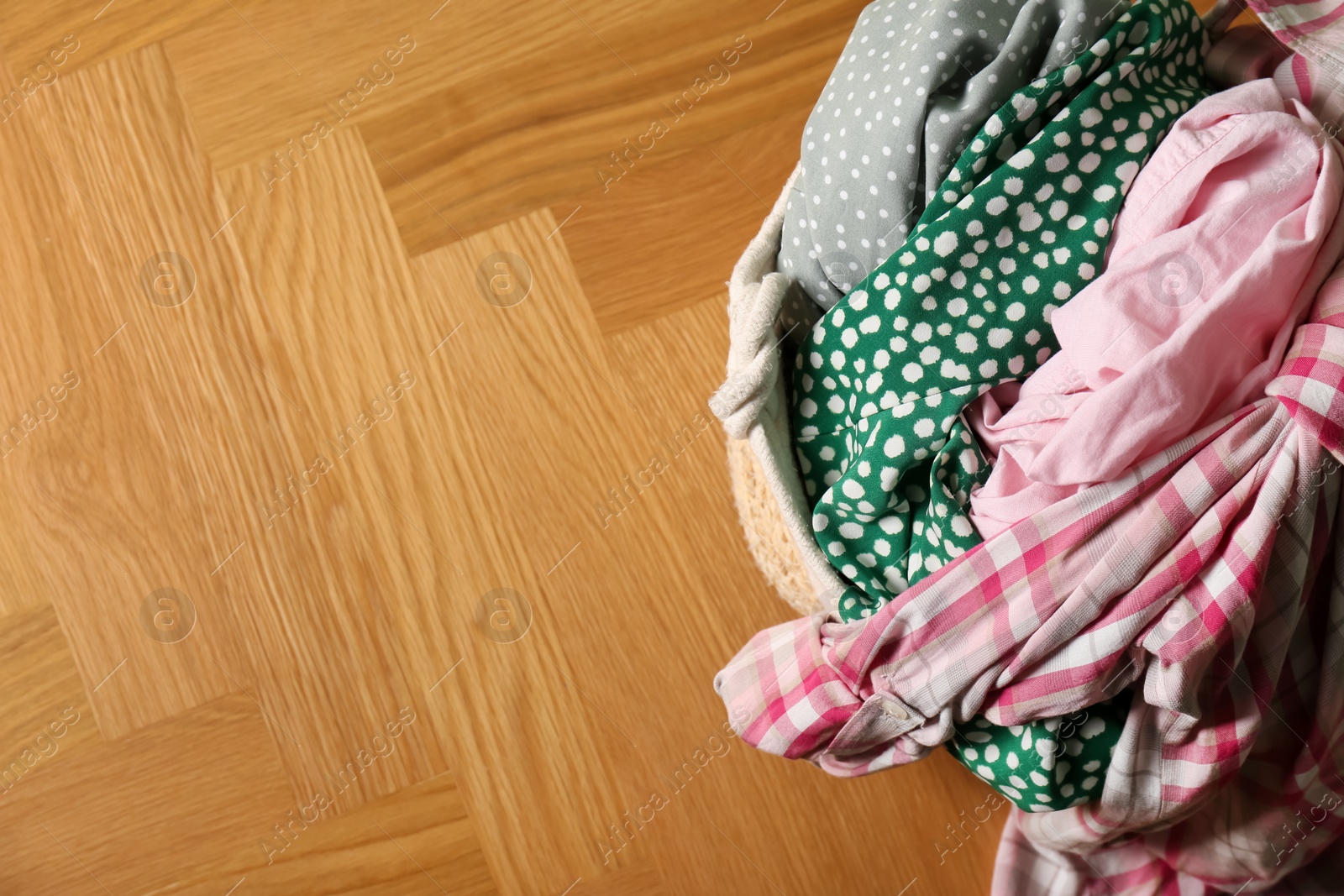 Photo of Laundry basket with clothes on floor, top view. Space for text