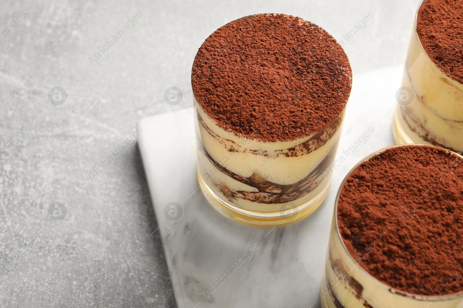 Photo of Delicious tiramisu in glasses on grey textured table, closeup. Space for text