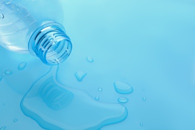 Drops of spilled water and plastic bottle on light blue background, closeup