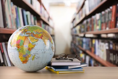 Globe, books and eyeglasses on wooden table in library. Space for text