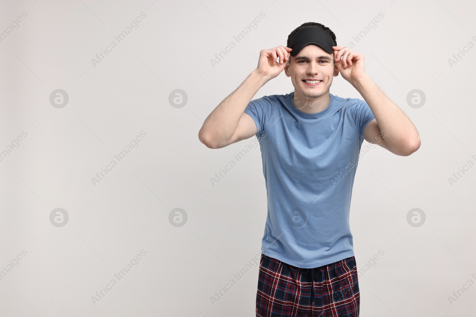 Photo of Happy man in pyjama and sleep mask on light grey background, space for text