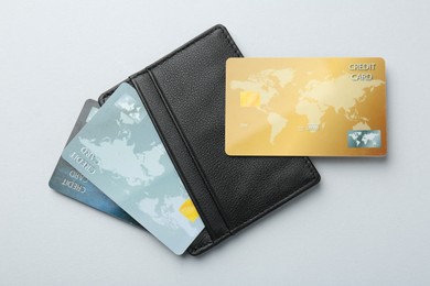 Woman holding leather card holder with credit cards on light grey background, top view