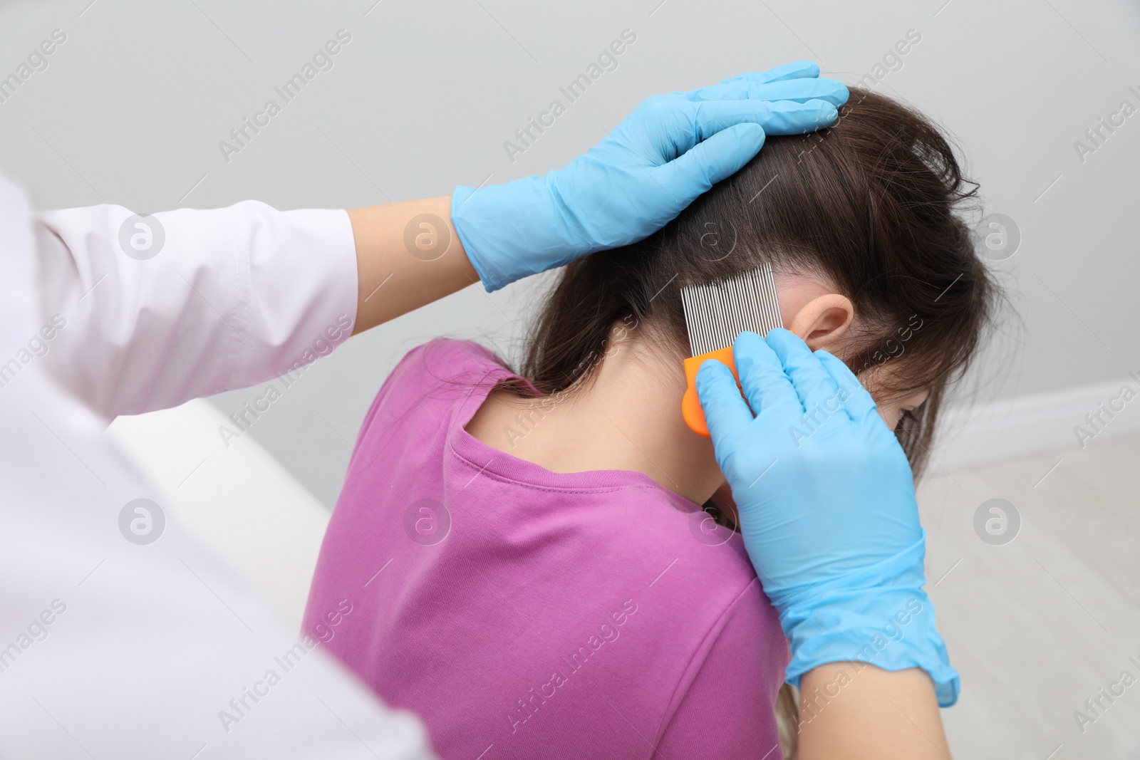 Photo of Doctor using nit comb on little girl's hair indoors. Anti lice treatment