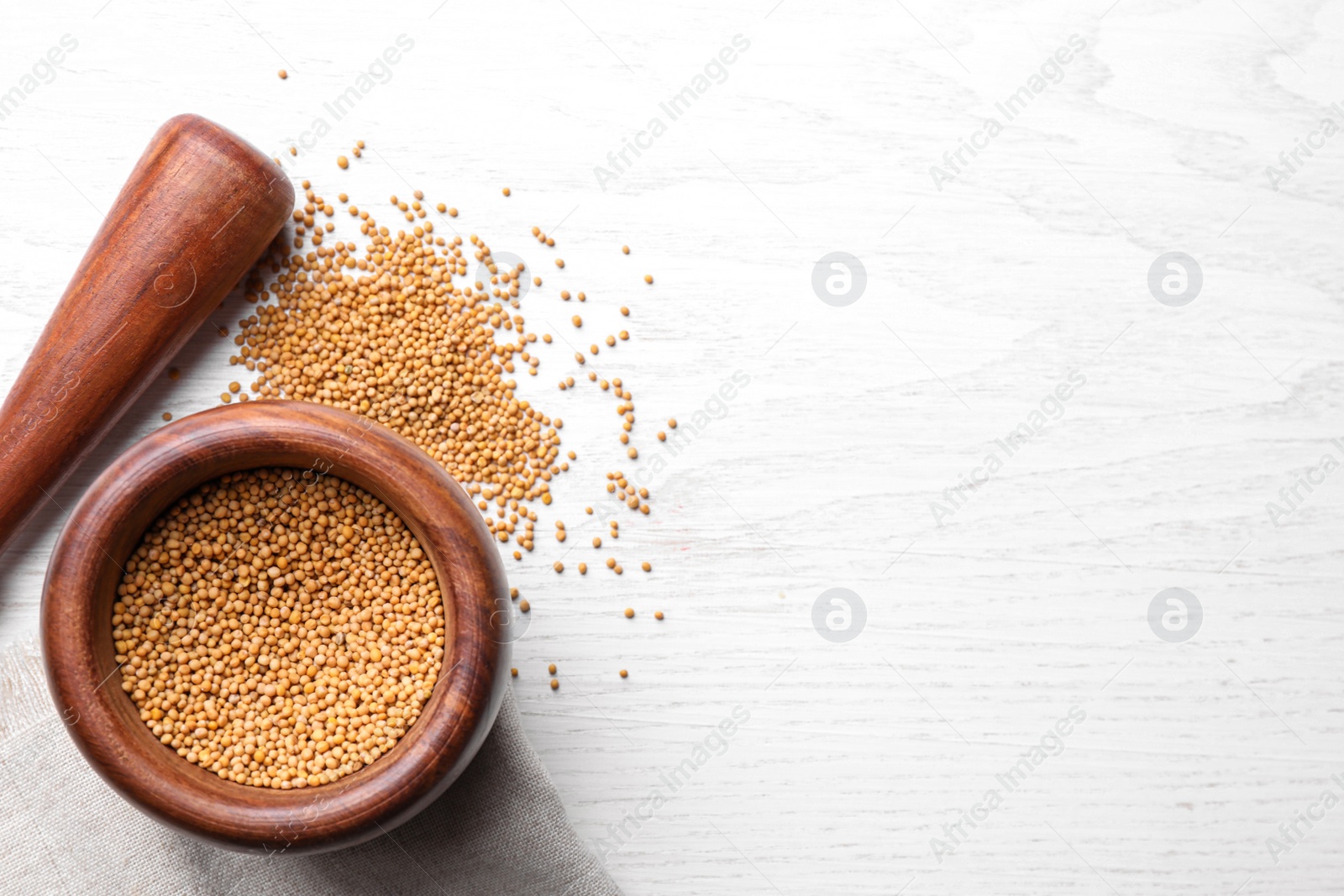 Photo of Mustard seeds with wooden mortar and pestle on white table, flat lay. Space for text