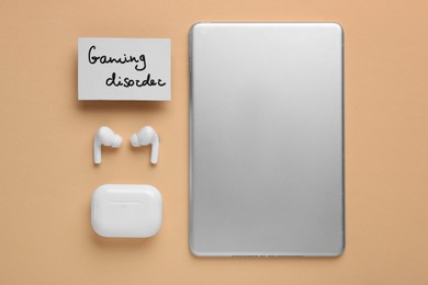 Card with phrase Gaming Disorder, earphones and tablet on beige background, flat lay. Addictive behavior