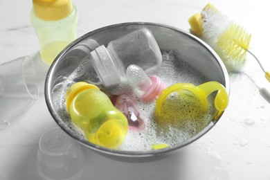 Metal bowl with baby bottles on white table