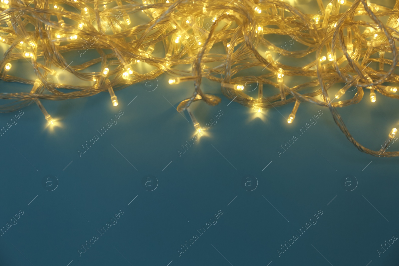 Photo of Glowing Christmas lights on blue background, top view. Space for text