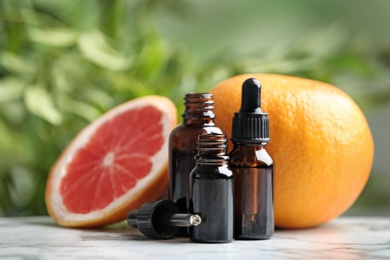 Photo of Bottles of essential oil and grapefruit on table against blurred background