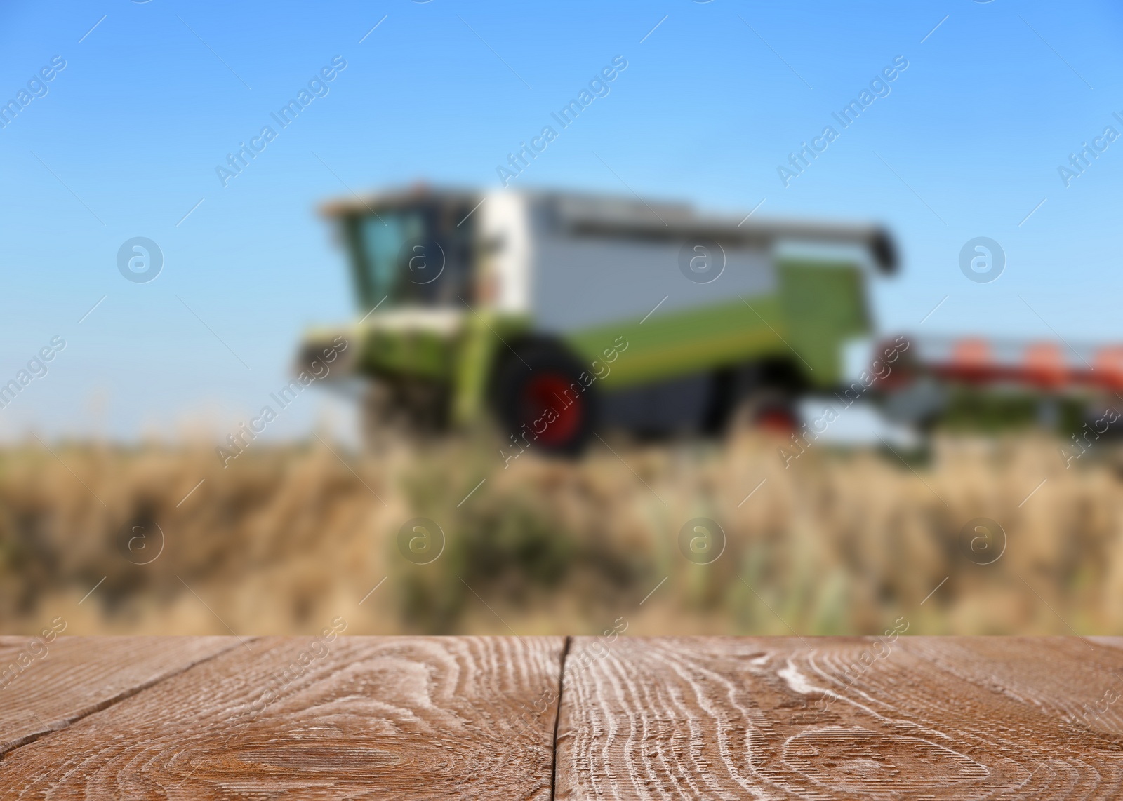 Image of Empty wooden surface and blurred view of modern combine harvester in wheat field. Space for text
