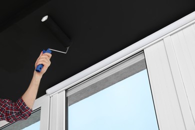 Worker painting ceiling with roller indoors, closeup