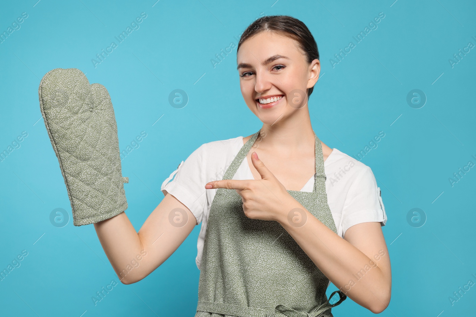 Photo of Beautiful young woman in clean apron with pattern and oven glove on light blue background